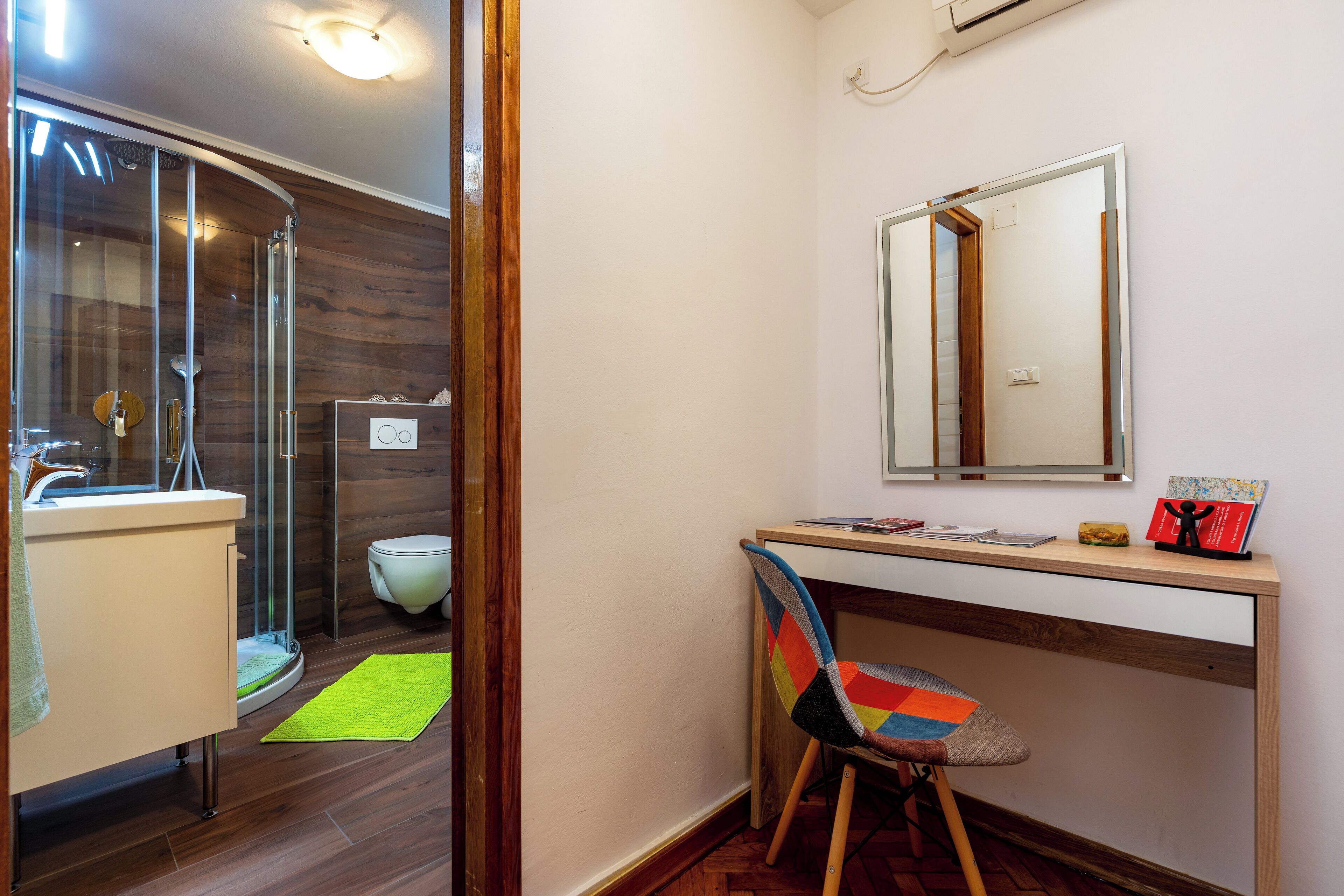 A modern bathroom with a glass shower enclosure, a toilet, and a desk with a chair.