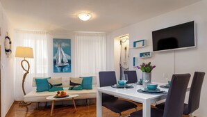 A modern living room with a sofa, dining table, and chairs. There is a painting on the wall, a lamp, and a TV mounted on the wall. - Sorgenfrei 2-bedroom apartment in Rovinj Old Town (Rovinj)
