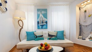 A living room with a sofa, a round coffee table with fruit, a painting of a sailboat, and a wall with a net and birds. - Sorgenfrei 2-bedroom apartment in Rovinj Old Town (Rovinj)