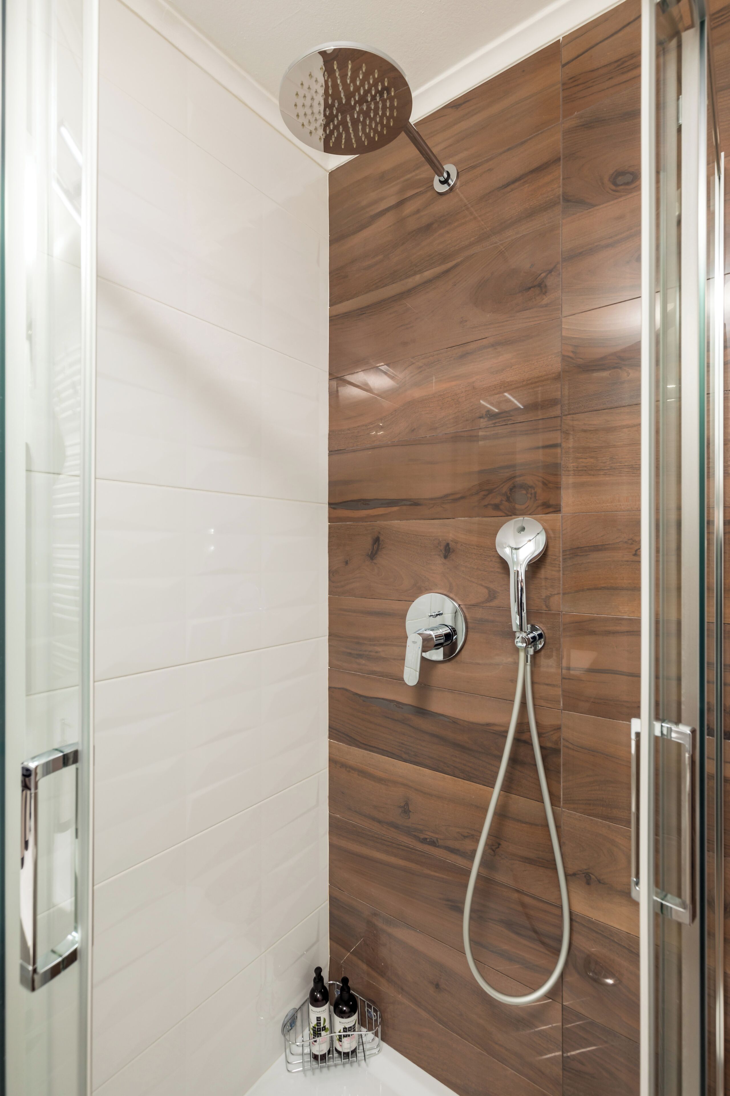 A modern shower with a wooden panel wall, a glass shower door, and a handheld showerhead.
