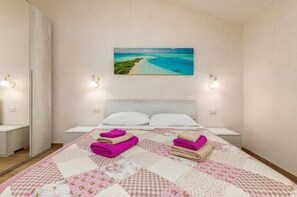 Una habitación de hotel con una cama, un cuadro de una playa y una mesita de noche con una lámpara.