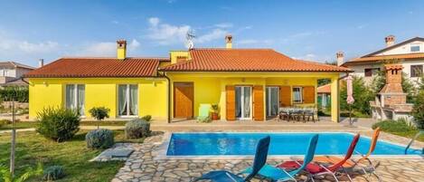 A two-story yellow house with a swimming pool and outdoor seating.