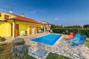 Una villa amarilla con piscina y mobiliario de exterior.