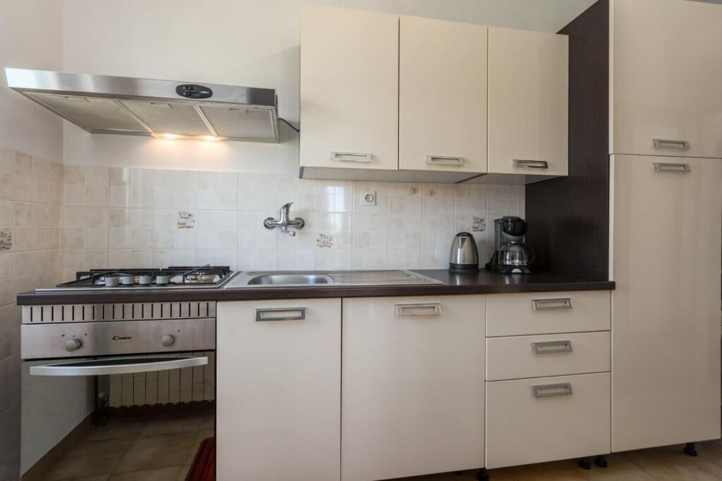 A modern kitchen with white cabinets, a stainless steel range hood, a gas stove, a sink, and a coffee maker.
