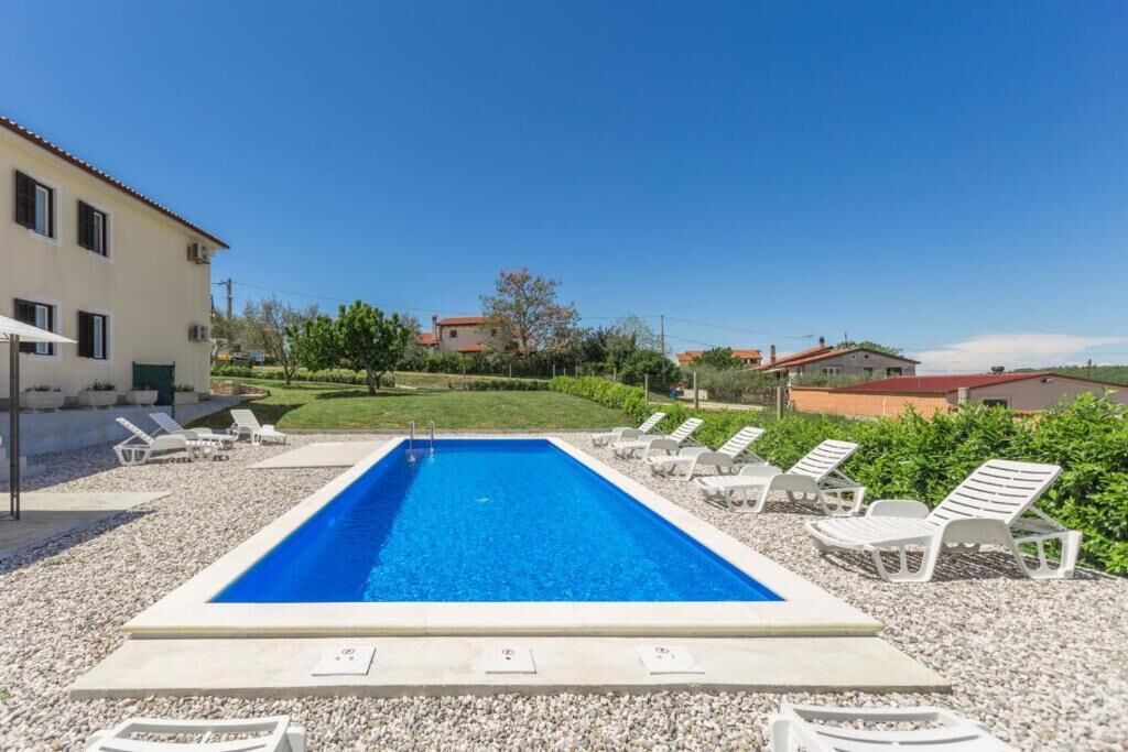 A rectangular swimming pool with clear blue water, surrounded by white lounge chairs and a gravel area.