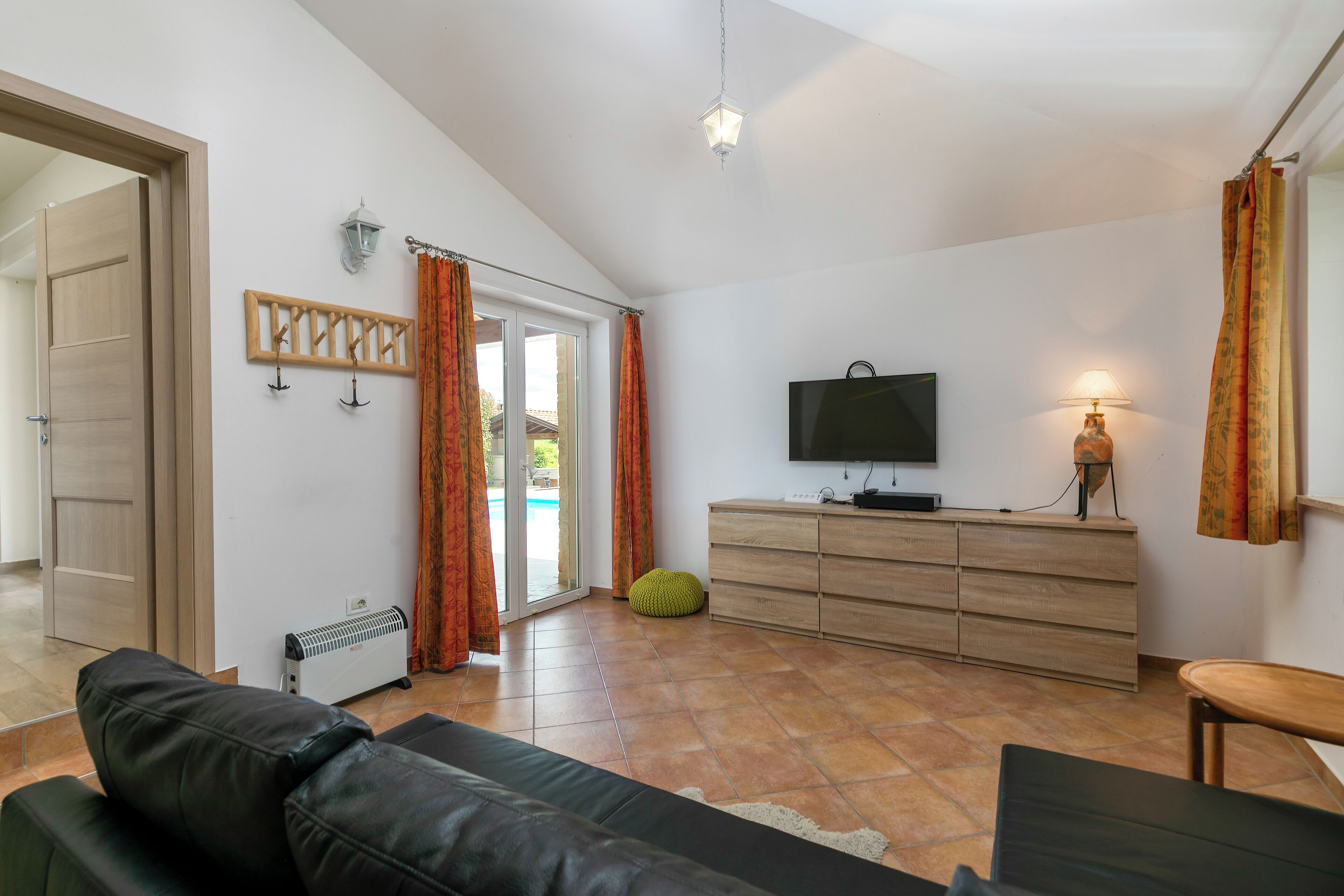 A modern living room with a leather sofa, a wooden cabinet, a television, and a lamp.