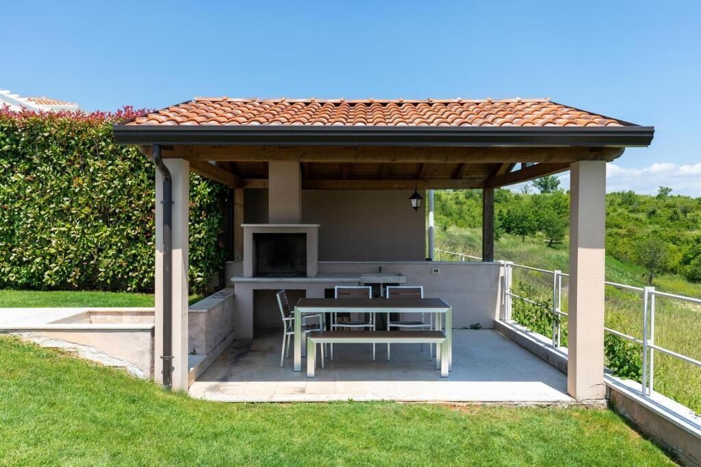 Un patio techado al aire libre con una parrilla, mesa y sillas.
