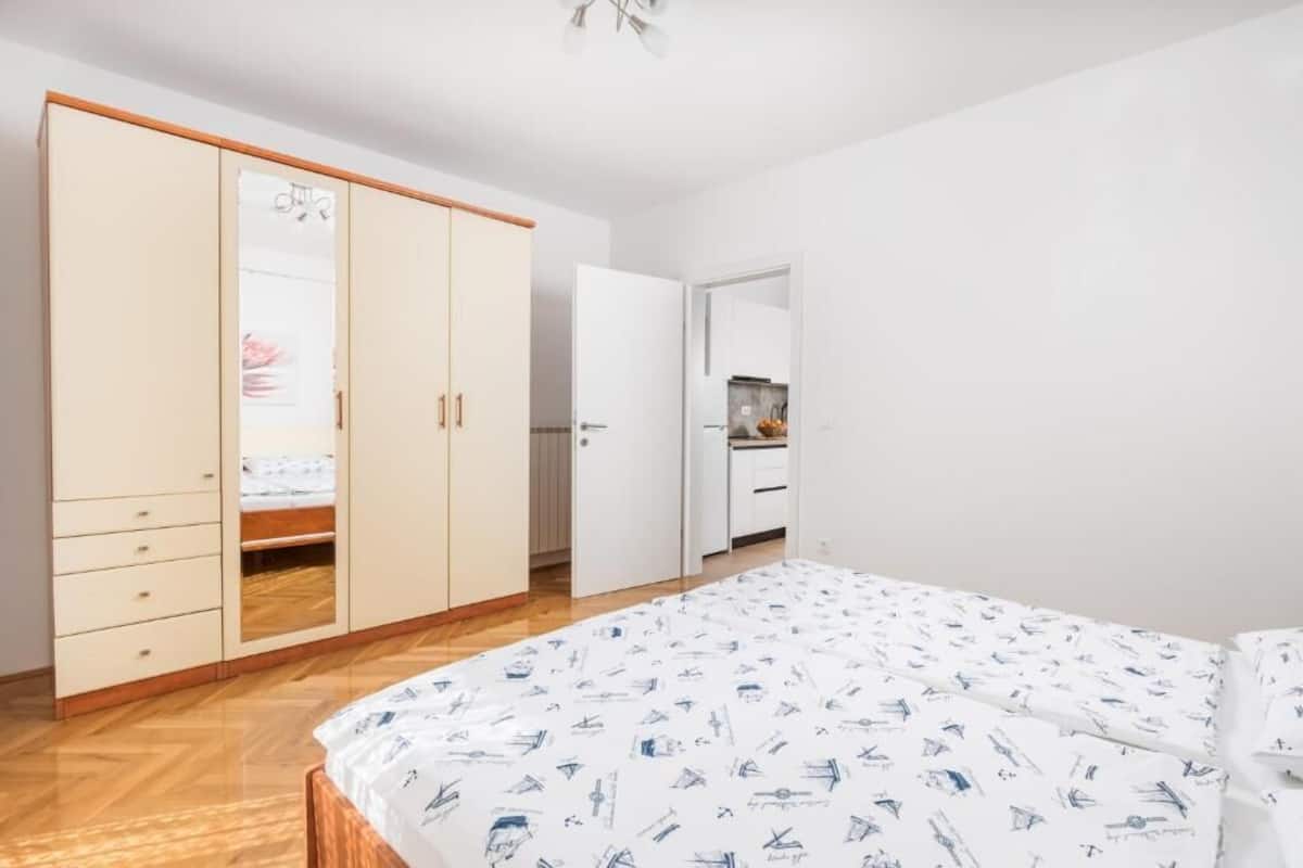 Ein Schlafzimmer mit großem Kleiderschrank, einem Bett mit gemustertem Überwurf und einer kleinen Küchenzeile.
