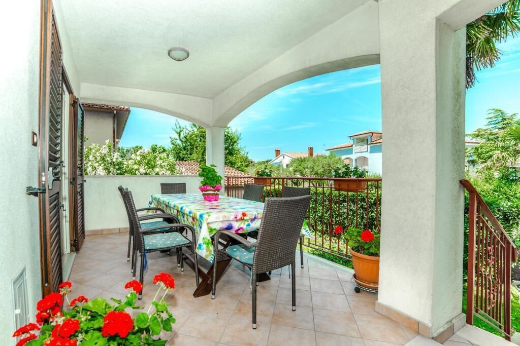 A covered patio with a table and chairs, potted plants, and a view of surrounding buildings.