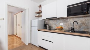 A modern kitchen with white cabinets, a black microwave, a sink, and a fruit bowl. - Guest House Marica (Rovinj)