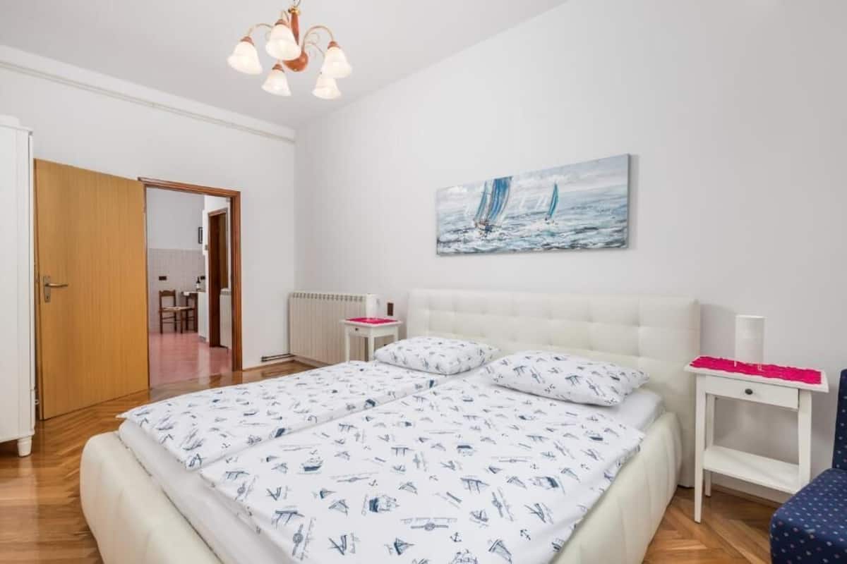Ein Schlafzimmer mit einem großen Bett, einem weißen Nachttisch, einem Gemälde von Segelbooten und einer Holztür.