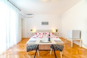 A bedroom with a bed, bedside tables, a small table with chairs, a TV, and a window with curtains. - Guest House Marica (Rovinj)