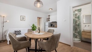 A compact living space with a round dining table, four chairs, a potted plant, and a small kitchen area. - Guest House Marica (Rovinj)