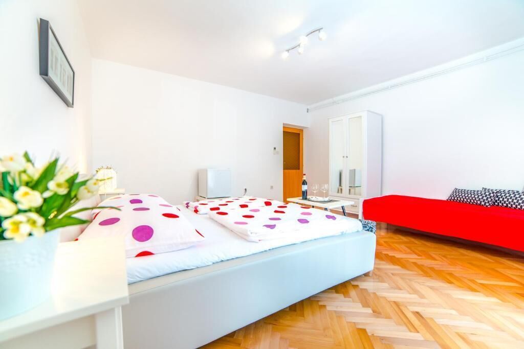 Une chambre d’hôtel moderne avec un lit, un canapé rouge, un plancher en bois et une petite table avec une lampe.