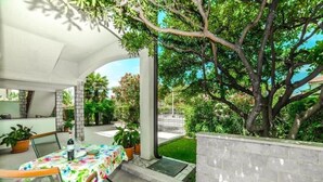 An outdoor patio with a table set for dining, surrounded by potted plants and a large tree. - Guest House Marica (Rovinj)