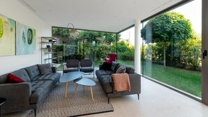 A modern living room with a sofa, chairs, and a coffee table. There is a large window providing a view of a garden. - Villa Rm (Rovinj)