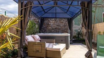 Relax in a secluded outdoor oasis with a hot tub and comfortable seating area under a shaded pergola.
