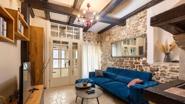 Ein gemütliches Wohnzimmer mit einer Steinwand, einem blauen Sofa, einem Holztisch und einem Fernseher auf einem Holzständer.