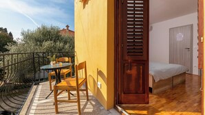 A small room with a bed, a wooden door, and a balcony with a table and chairs.