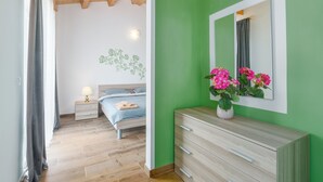A bedroom with a wooden ceiling, a bed with a blue and white patterned bedspread, a nightstand with a lamp, and a dresser with a mirror and flowers. - Villa Diletta (Kanfanar)