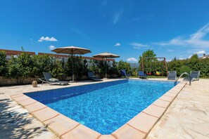 Ein rechteckiger Pool mit Fliesenrand, umgeben von Liegestühlen und Sonnenschirmen, vor einem strahlend blauen Himmel.