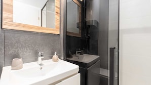 Une salle de bain moderne avec un lavabo blanc, un miroir et une cabine de douche en verre.