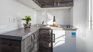 Une cuisine de taille réduite avec des meubles de couleur bois foncé, un plan de travail blanc, un évier encastré et un réfrigérateur.