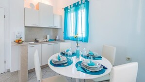 Una cocina moderna con armarios blancos, un lavamanos y una encimera con un frutero. Hay una mesa de comedor con individuales azules y platos blancos.