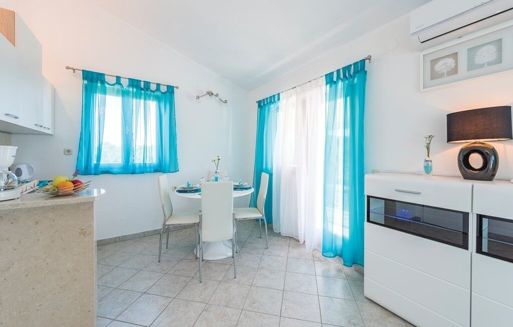 A small, bright kitchen with white cabinets, a dining table with chairs, and blue curtains.
