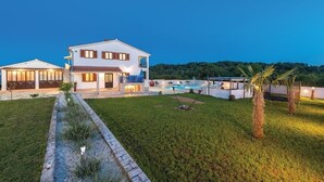 Una casa de dos pisos con piscina, césped cuidado y vista a un área boscosa.
