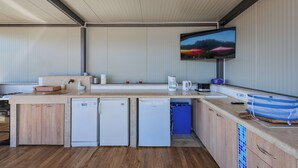 Cocina compacta con lavavajillas integrado, cafetera y televisor de pantalla plana montado en la pared.