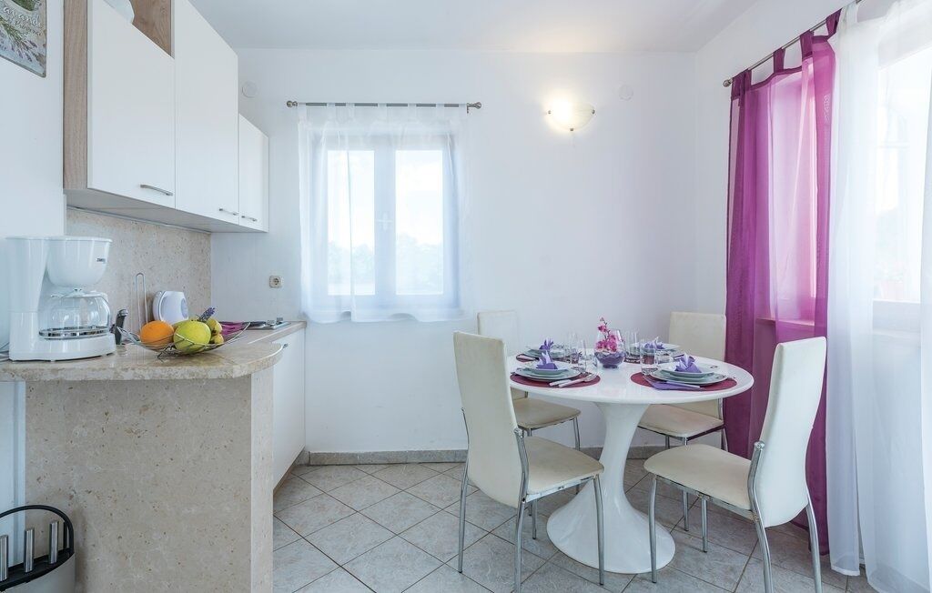 Une petite cuisine lumineuse, avec des meubles blancs, une machine à café et un coin repas comprenant une table ronde et quatre chaises.