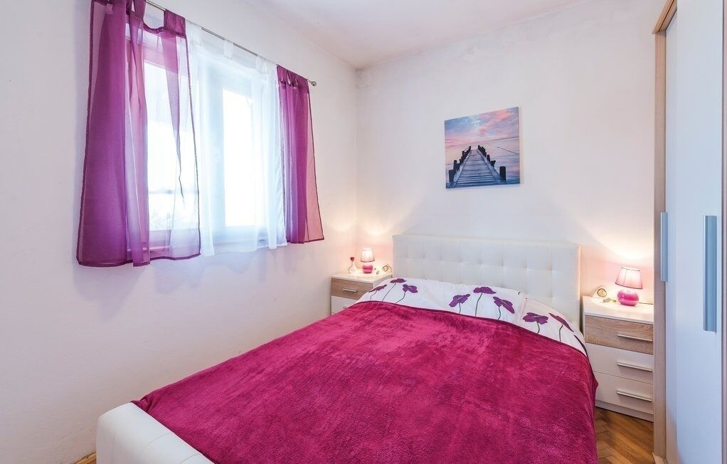 A bedroom with a bed, a nightstand, a lamp, a window with curtains, and a painting on the wall.