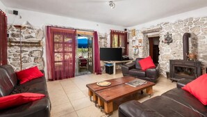 Una sala de estar con paredes de piedra, una chimenea, sofás de cuero con cojines rojos, una mesa de centro de madera y un televisor.