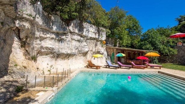 Una piscina con un acantilado rocoso de fondo, sillas de descanso y sombrillas.