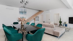 Ein modernes Wohnzimmer mit einem Glastisch, Smaragdgrünen Stühlen, einem beigen Sofa und einer Treppe.
