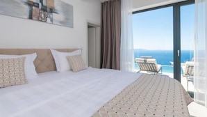 Ein Hotelzimmer mit einem großen Bett, Meerblick und einem Balkon mit Sitzgelegenheiten.