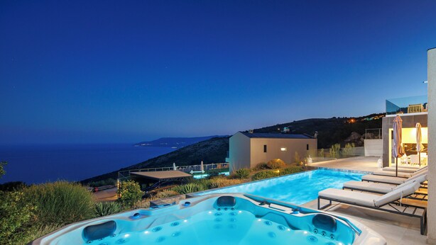 Ein Whirlpool mit Blick auf den Pool, Liegestühle und ein Gebäude mit einem Balkon mit Meerblick.