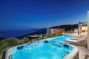 Boblebad med udsigt til poolen, liggestole og en bygning med balkon over havet.