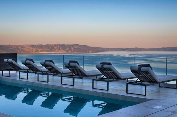 A poolside area with lounge chairs facing a body of water and distant hills. - Villa Ultima (Labin)