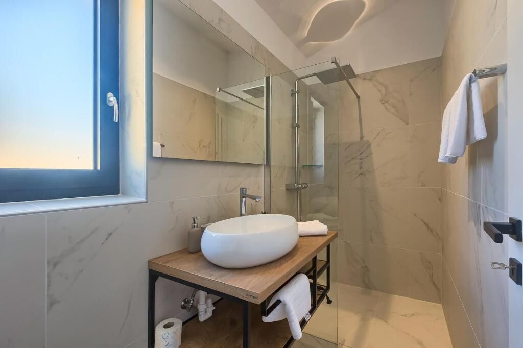 A modern bathroom with a large oval sink, a glass shower enclosure, and a large mirror.