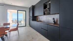 A modern kitchen with dark cabinetry, a large window, and a view of the ocean. - Villa Ultima (Labin)