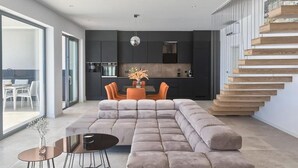 A modern living room with a sectional sofa, a dining area with orange chairs, and a kitchen in the background. - Villa Ultima (Labin)