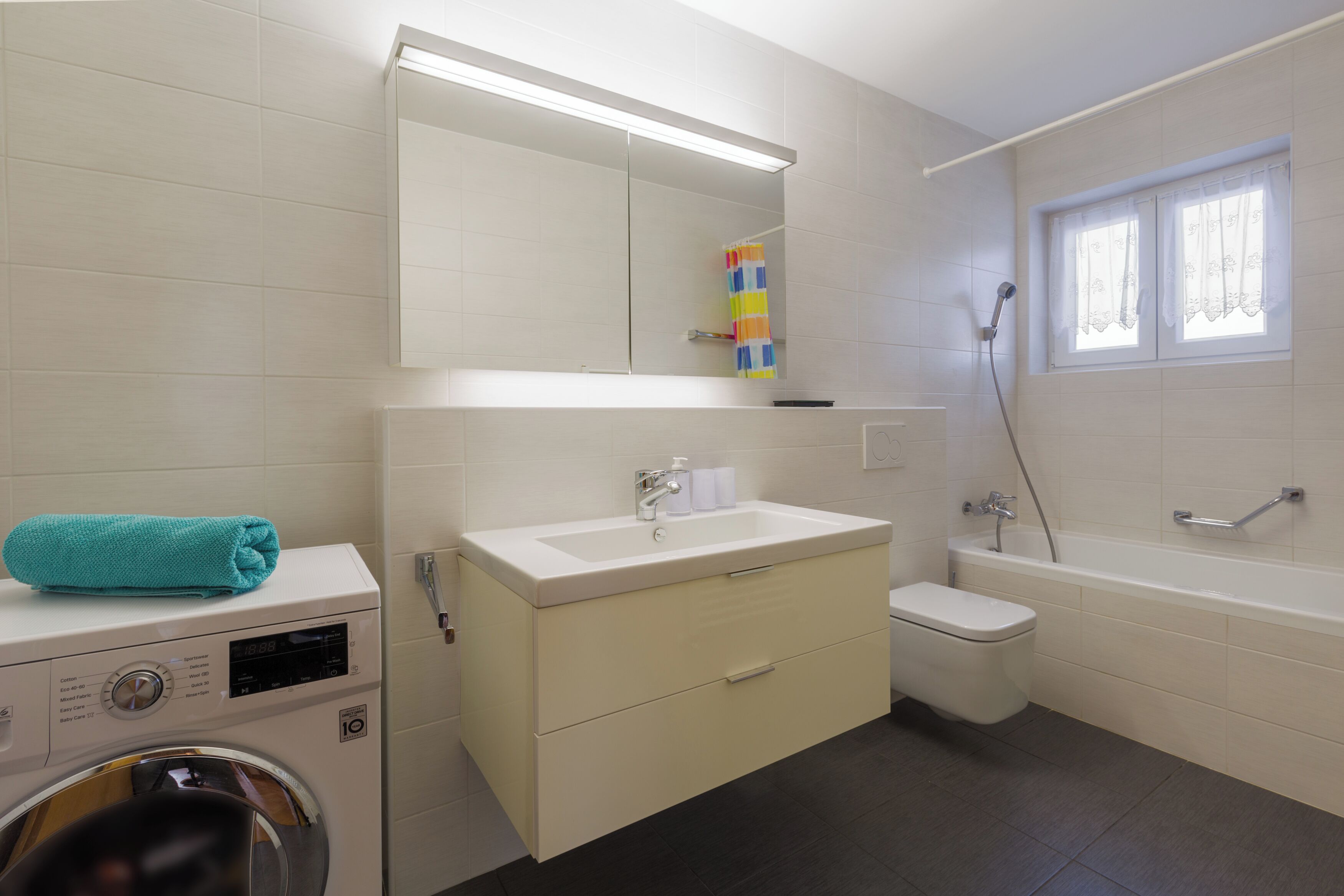 Une salle de bain moderne équipée d’une machine à laver, d’un lavabo, de toilettes et d’une baignoire.