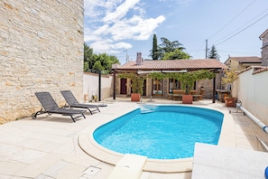 A swimming pool with lounge chairs, a stone wall, and a covered patio area. - Villa Diana (Kanfanar)