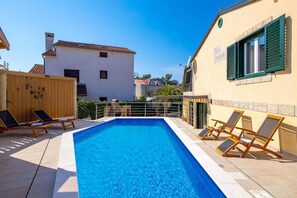 A swimming pool with lounge chairs, a wooden fence, and a building with a tiled roof in the background. - Villa Ivona (Rovinj)