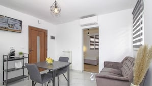 A modern living room with a sofa, a dining table with chairs, a coffee machine, and a decorative vase. - Apartments Doris (Rovinj)
