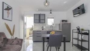 A modern kitchen with a dining area, a grey sofa, and a TV mounted on the wall. - Apartments Doris (Rovinj)