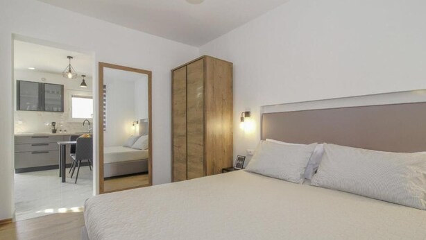 A bedroom with a bed, a wardrobe, a bedside table, and a nightstand. There is a door leading to a bathroom and a kitchenette. - Apartments Doris (Rovinj)
