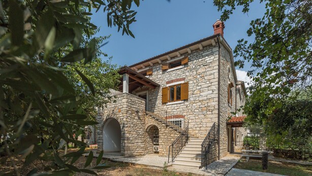 A stone building with a staircase leading to a door, surrounded by trees.